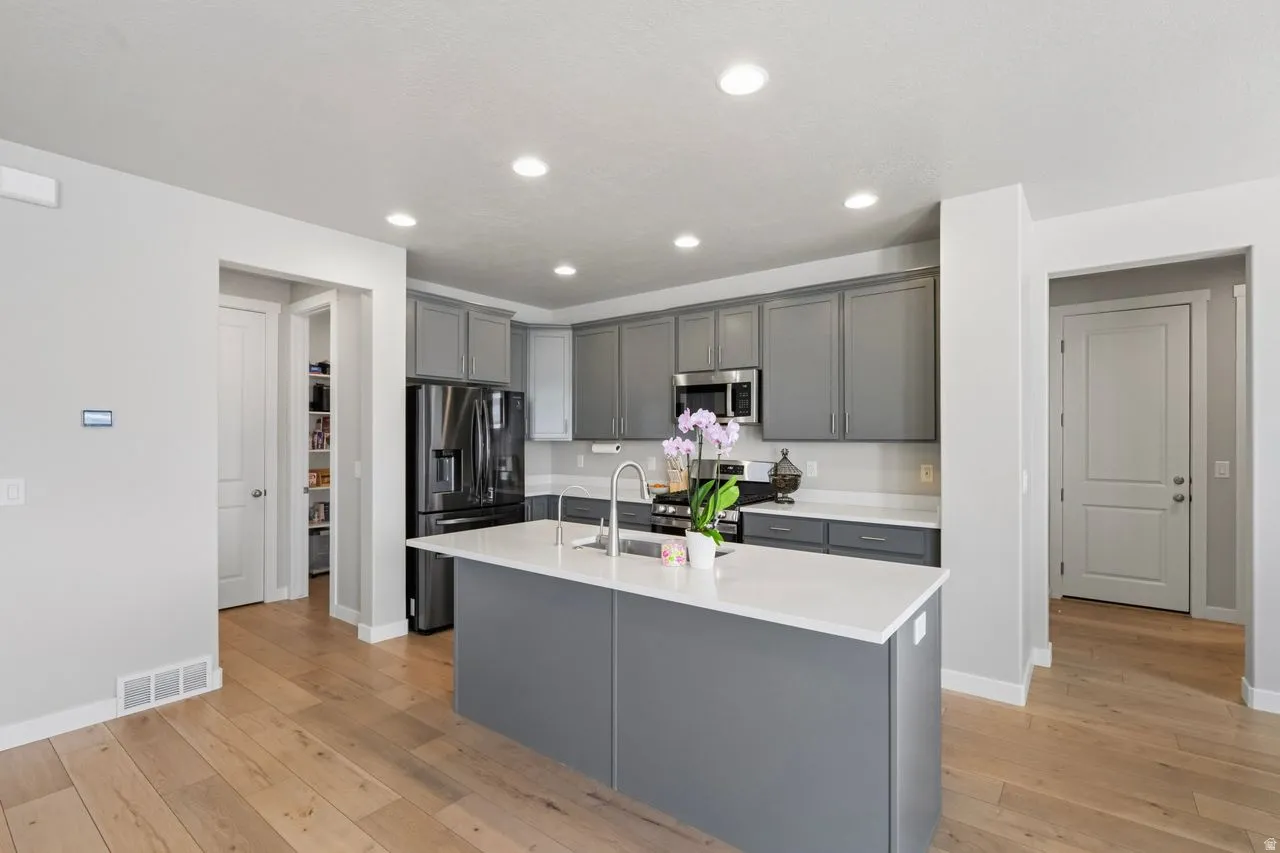 Kitchen featuring gray cabinets, stainless steel appliances, light wood-style floors, a center island with sink, and recessed lighting