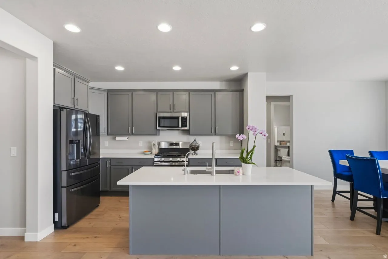 Kitchen with gray cabinets, stainless steel appliances, light wood finished floors, an island with sink, and recessed lighting