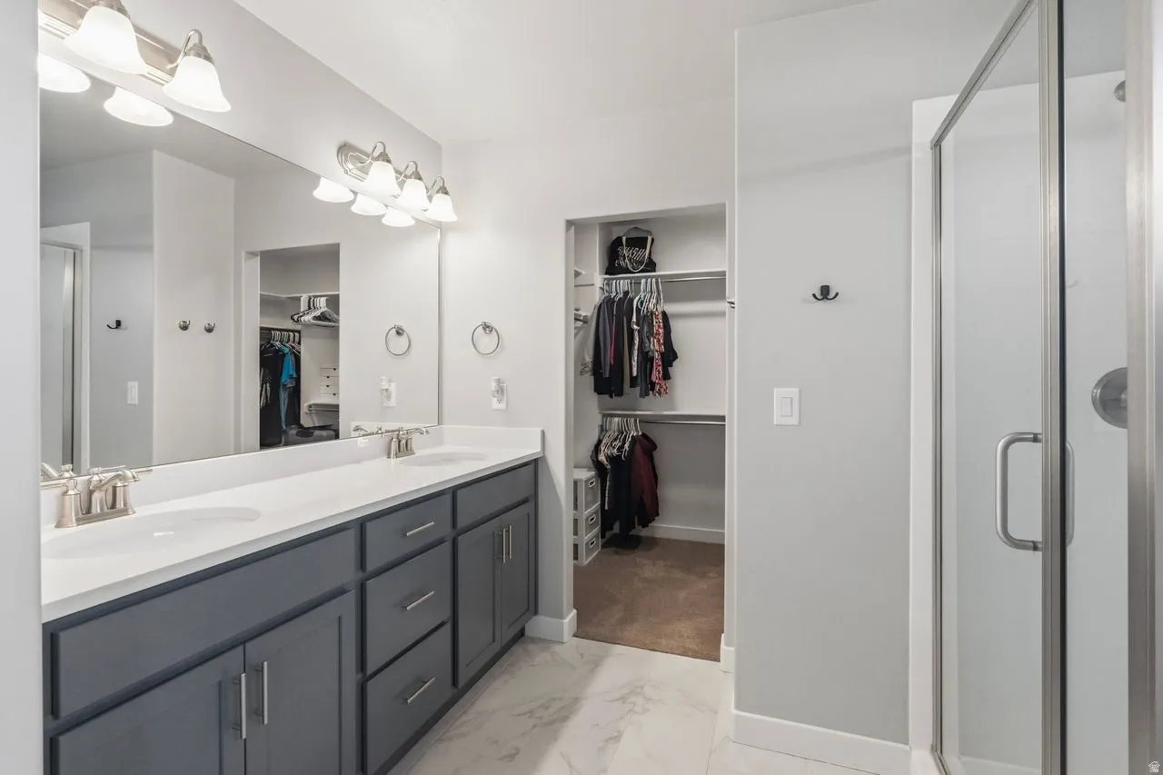 Bathroom featuring a shower stall, double vanity, light marble finish flooring, and a walk in closet