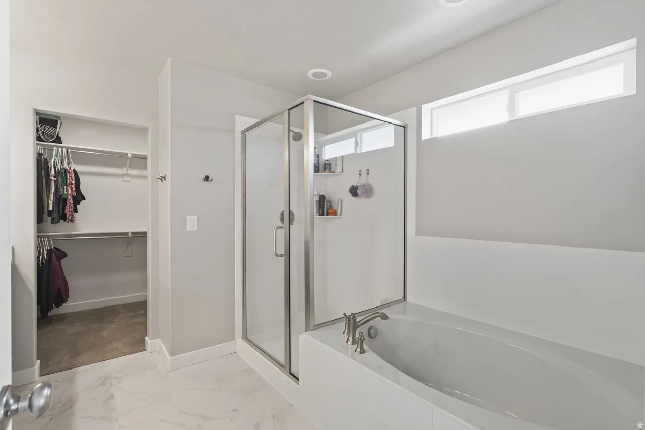 Bathroom with a walk in closet, a stall shower, a bath, and light marble finish floors