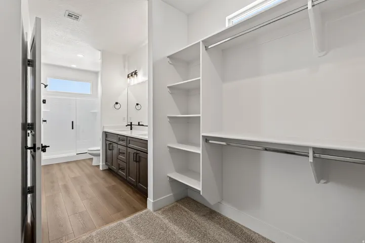 Walk-in closet featuring white shelving, multiple hanging rods, and an integrated transom window