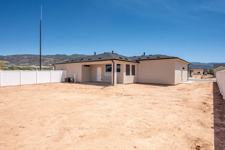 Spacious backyard with a white vinyl privacy fence, concrete patio, and stucco exterior