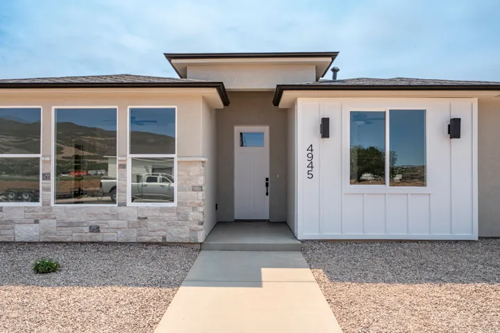 Modern stucco exterior featuring a white board and batten accent wall, stone veneer detailing, and a prominent front entry with a transom window