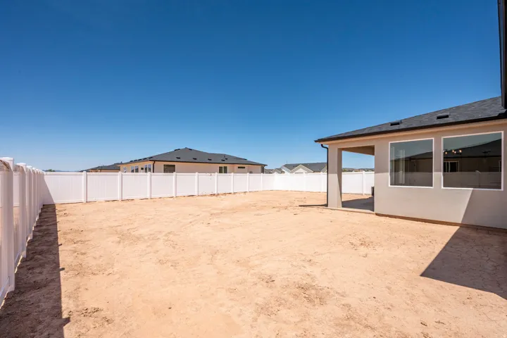 Spacious backyard featuring a covered patio, two large exterior windows, and a full-perimeter white vinyl fence