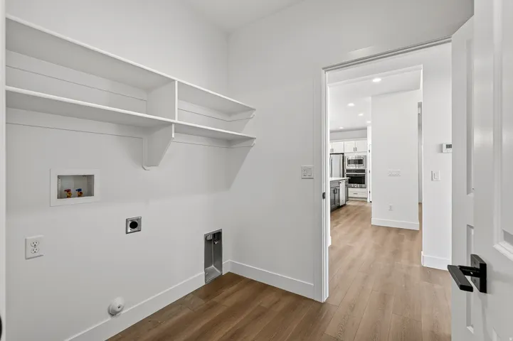Dedicated laundry area featuring built-in shelving, white walls, and wood-finish flooring