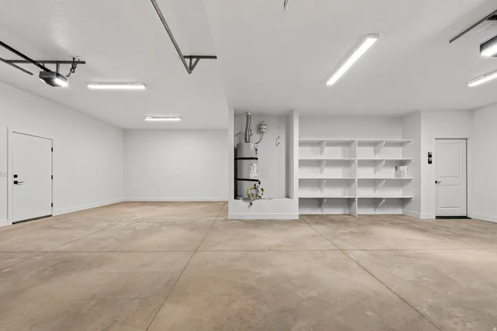 Spacious garage featuring concrete flooring, integrated shelving, bright overhead lighting, and white interior doors