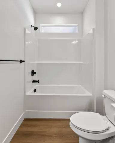 White bathtub and shower combination with matte black fixtures, set against wood-finish flooring