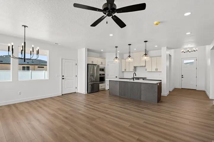 Open-concept living space featuring wood-finish flooring, a modern kitchen island with pendant lighting, stainless steel appliances, and a contemporary chandelier