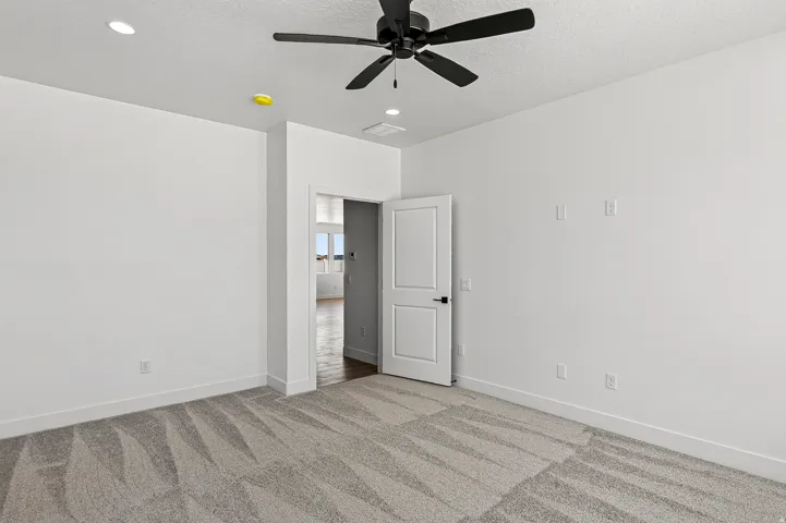Spacious room featuring patterned carpet, bright white walls, recessed lighting, and a ceiling fan