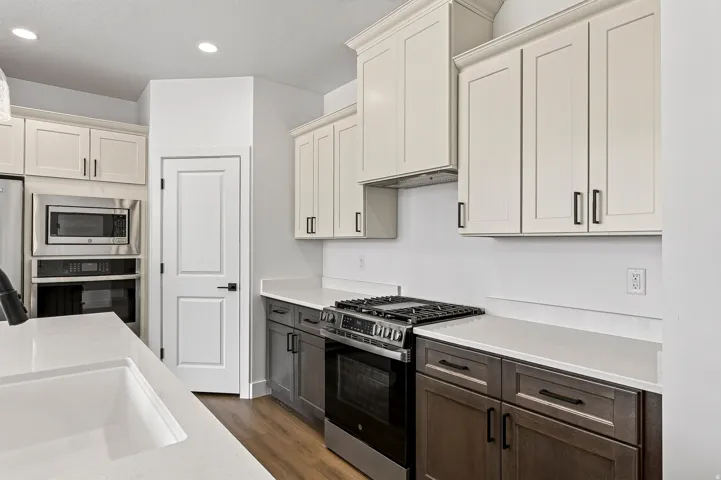 Modern kitchen featuring a gas range with a stainless steel oven, white countertops, and wood-finish flooring