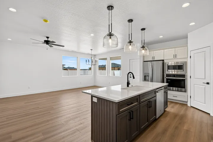 Open-concept kitchen and living area featuring wood-finish flooring, a kitchen island with a white countertop and dark cabinetry, stainless steel appliances, and recessed lighting