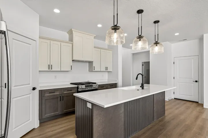 Kitchen featuring a central island with a built-in sink and matte black faucet, pendant lighting, two-tone cabinetry, stainless steel range, and wood-finish flooring