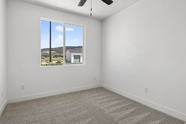 Bedroom featuring a large window, neutral carpeting, white walls, white baseboards, and a ceiling fan