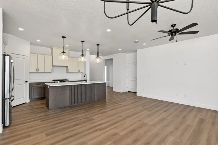 Open-concept living space featuring wood-finish flooring, a contemporary kitchen island with pendant lighting, stainless steel refrigerator, white cabinetry, and a ceiling fan