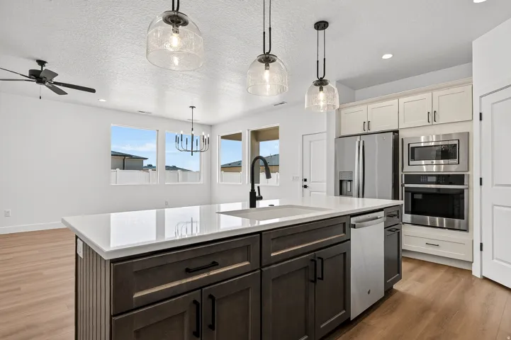 Modern kitchen featuring a large island with a white countertop and dark cabinetry, stainless steel appliances, wood-finish flooring, and contemporary pendant lighting