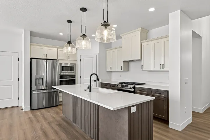 Kitchen featuring a central island with a solid surface countertop, stainless steel appliances, two-tone cabinetry, wood-finish flooring, and pendant lighting