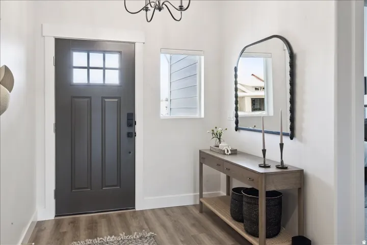 Entryway featuring a dark paneled door with glass inserts, wood-finish flooring, a decorative chandelier, a rectangular window with white trim, and white wall finishes