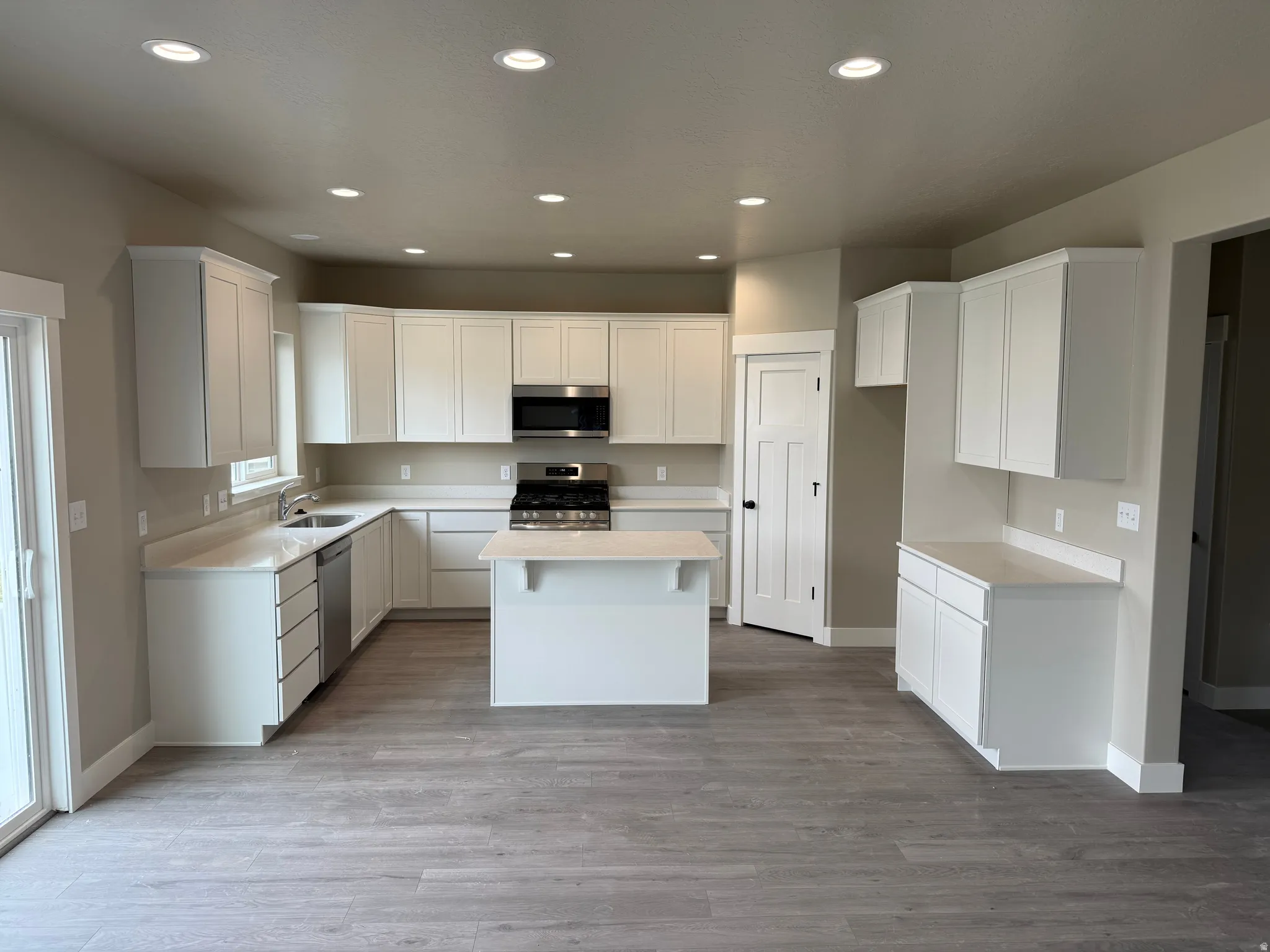 Kitchen featuring stainless steel appliances, recessed lighting, white cabinetry, light wood finished floors, and a center island