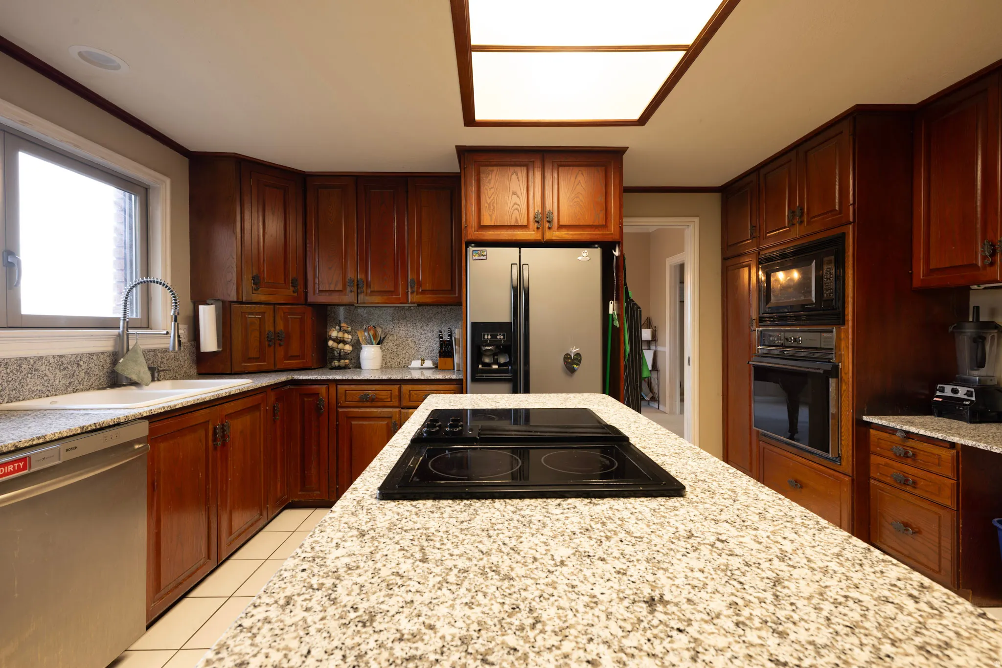 Kitchen with black appliances, light stone counters, light tile patterned floors, and decorative backsplash