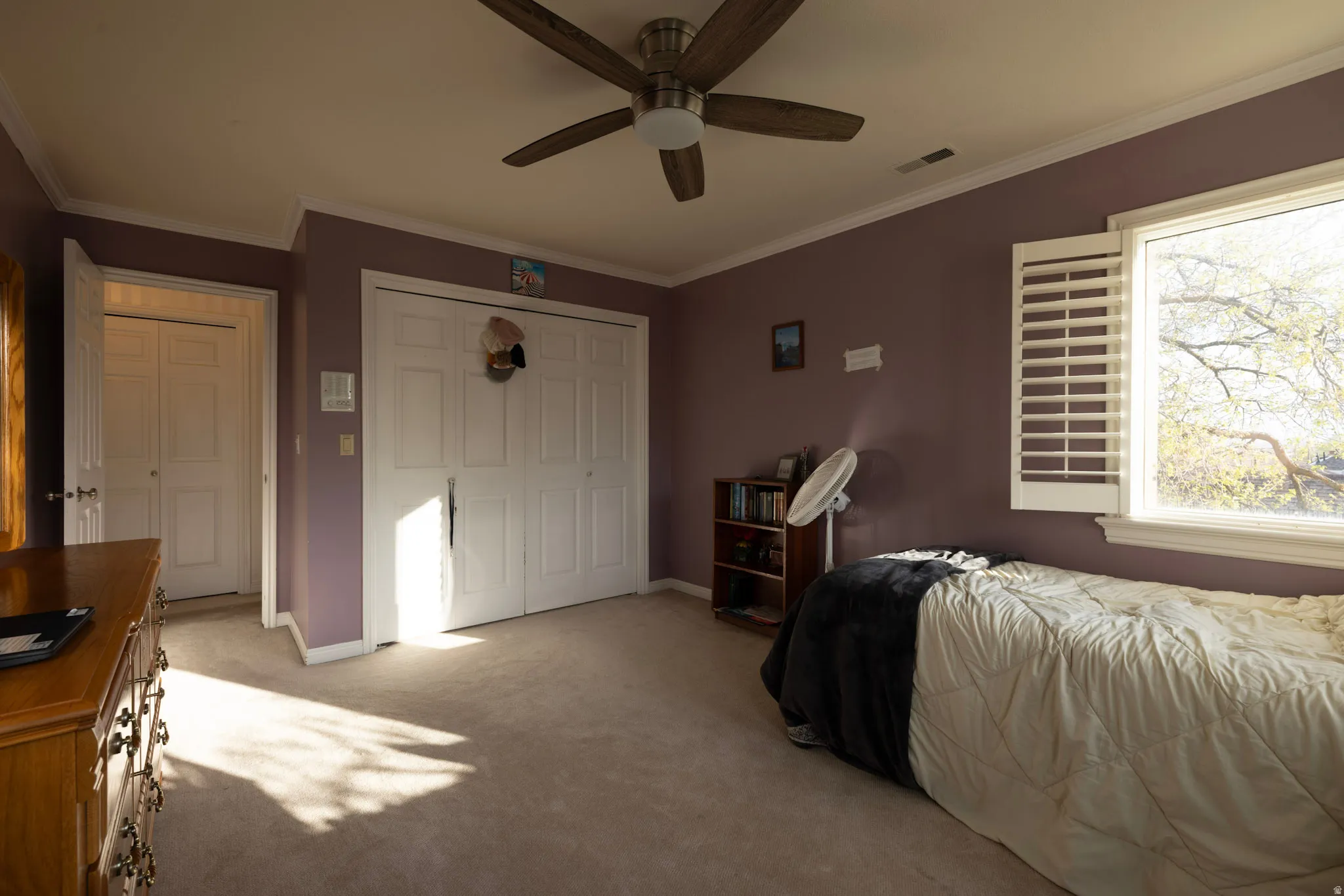 Bedroom with crown molding, a closet, light carpet, and a ceiling fan
