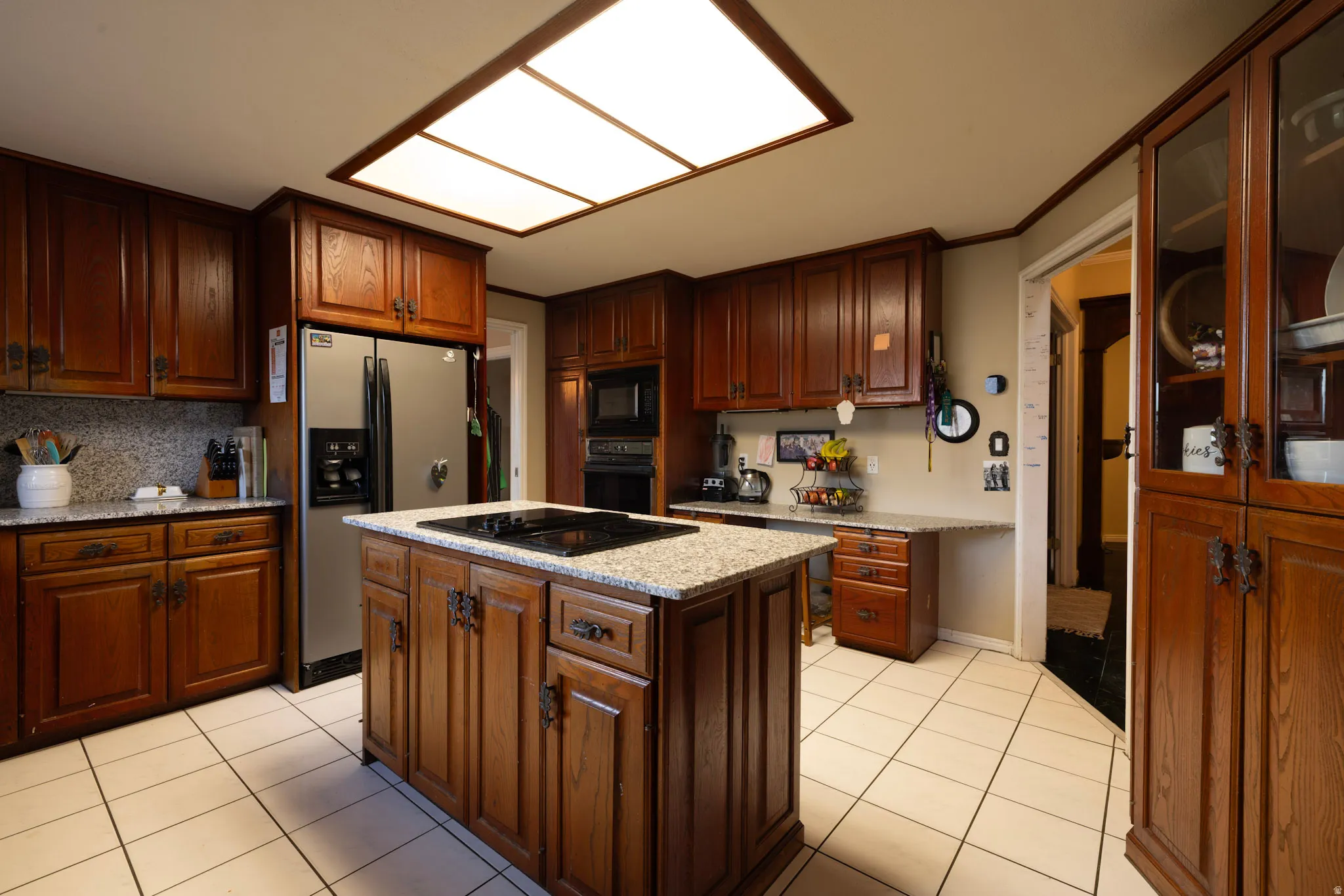 Kitchen featuring a center island, black appliances, light stone countertops, light tile patterned floors, and crown molding