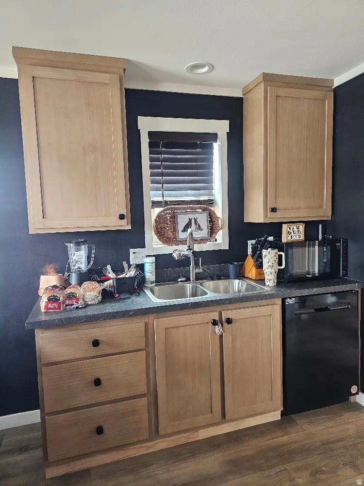 Kitchen with dark countertops, black dishwasher, dark wood-style flooring, and light wood finish cabinets