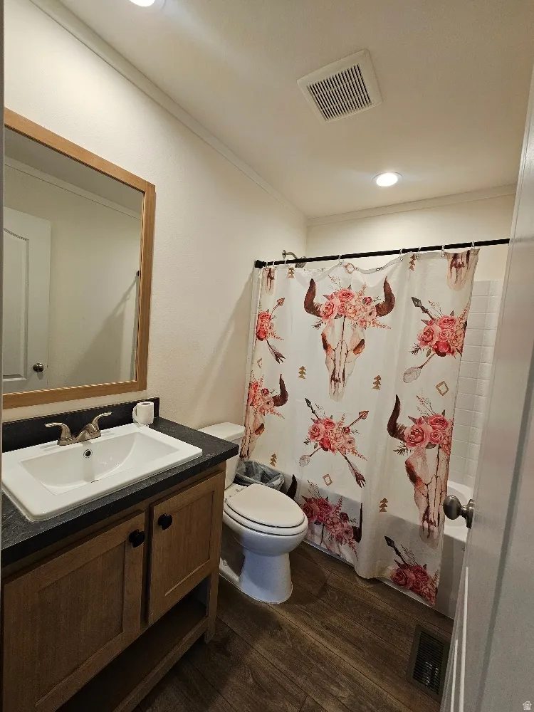Full bathroom featuring vanity, dark wood finished floors, shower / tub combo with curtain, ornamental molding, and recessed lighting
