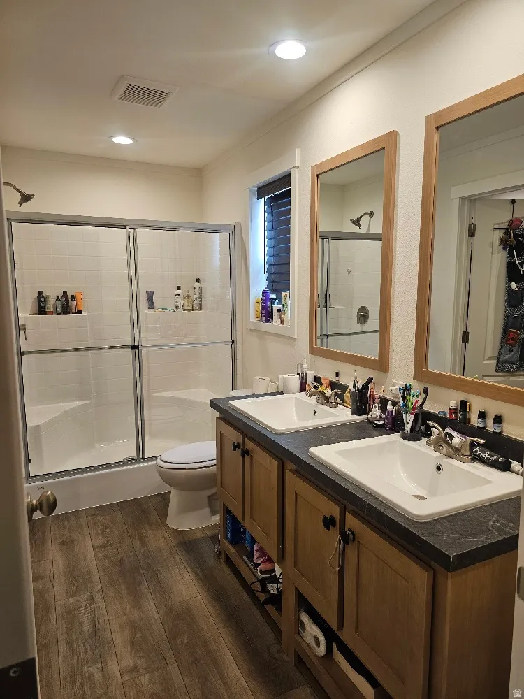 Master Bath F featuring dark wood finished floors, double vanity, a shower stall, and crown molding