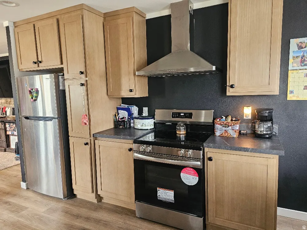 Kitchen with stainless steel appliances, dark countertops, light wood finish cabinetry, and light wood finished floors