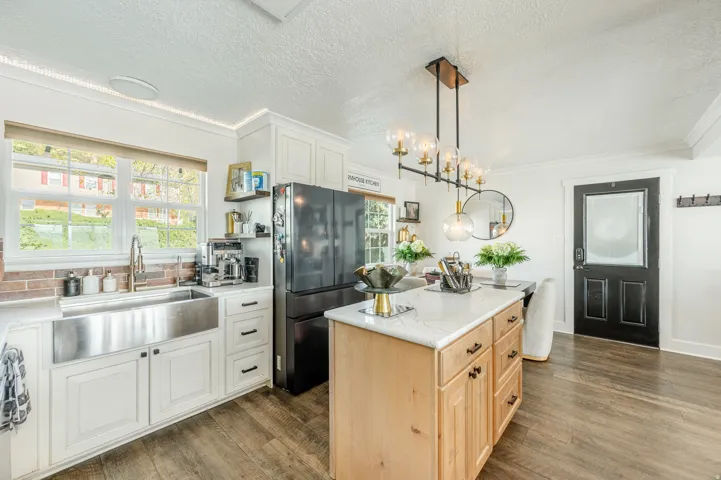 Kitchen featuring freestanding refrigerator, two tone cabinetry, dark wood-style floors, a center island, and ornamental molding