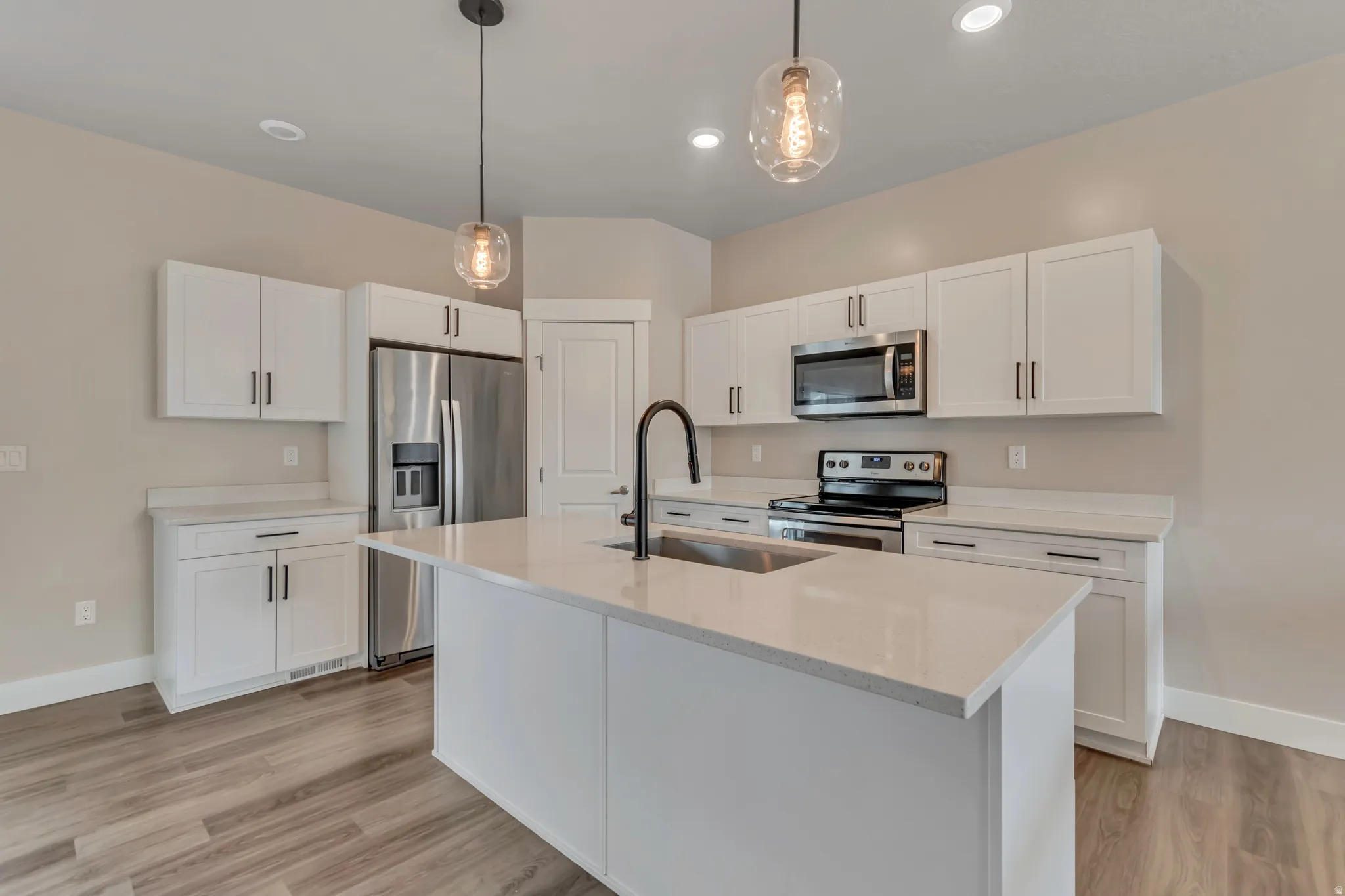Kitchen with stainless steel appliances, two-tone finishes, a center island with sink and island seating, pendant lighting, and white cabinetry