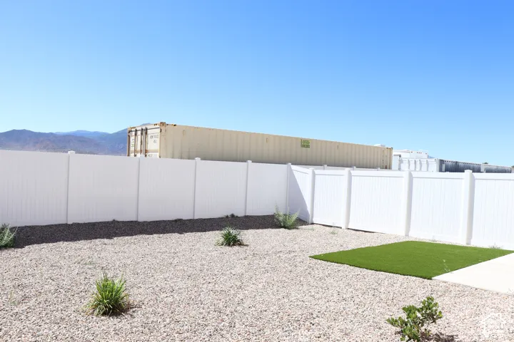 Low-maintenance backyard featuring gravel landscaping, a white privacy fence, and a square of artificial turf