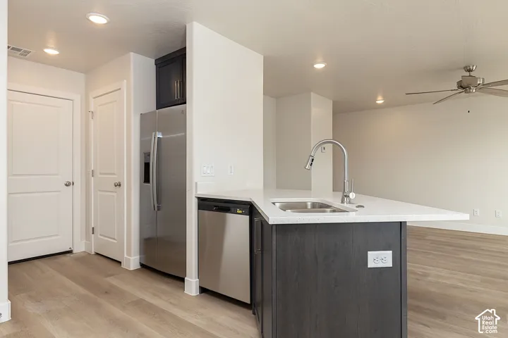 Kitchen featuring stainless steel appliances, a peninsula, ceiling fan, light wood finished floors, and light stone countertops