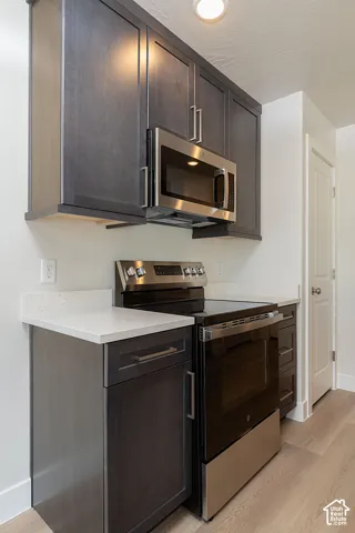 Kitchen featuring stainless steel appliances, light wood-style floors, dark wood finish cabinets, and light stone counters