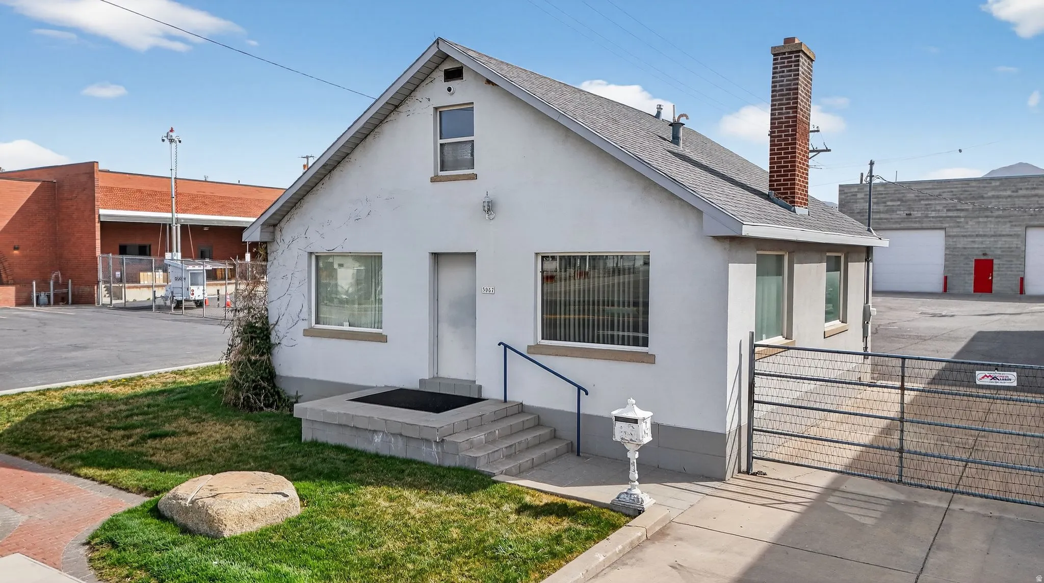 Bungalow-style home featuring a chimney, stucco siding, a shingled roof, and a gate