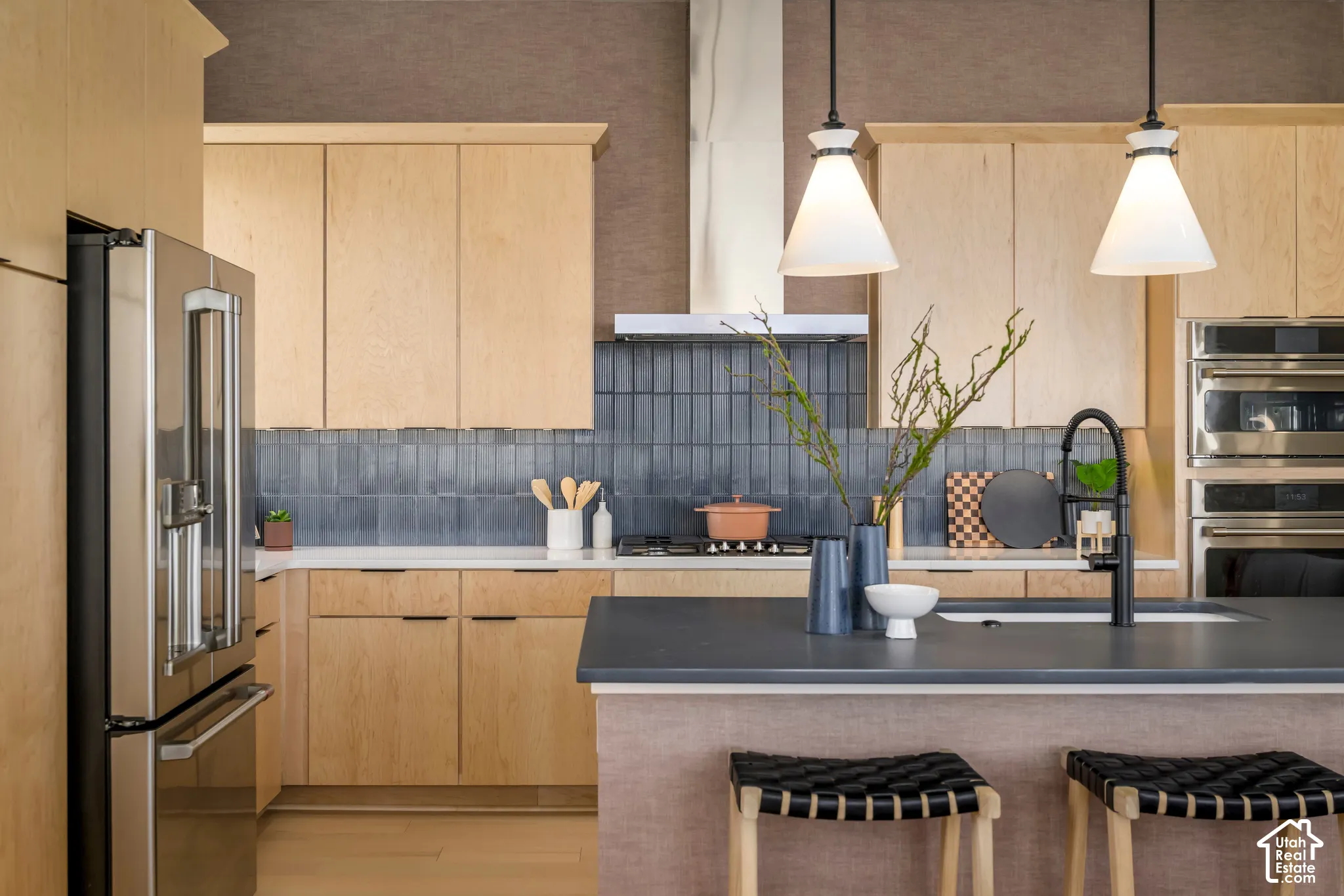 Kitchen featuring flat-panel wood cabinetry, dark vertical-tile backsplash, stainless steel built-in appliances, quartz countertops, and dual pendant lighting