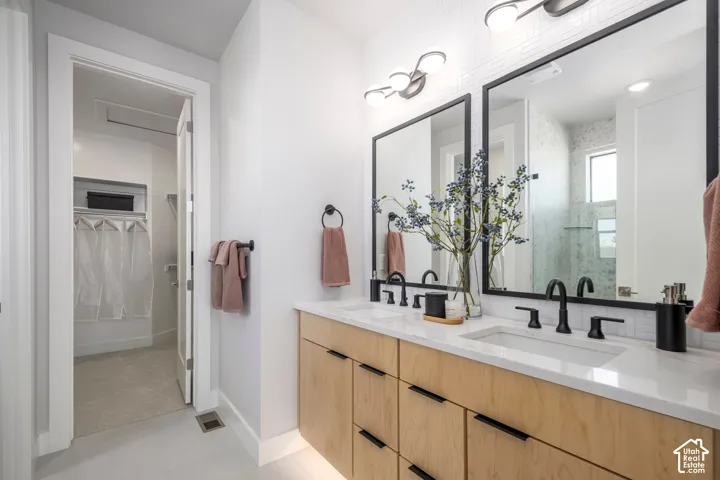 Dual-sink vanity with light-tone wood-finish cabinetry, white countertop, rectangular undermount sinks, black matte hardware, and dual framed mirrors with multi-light wall fixtures