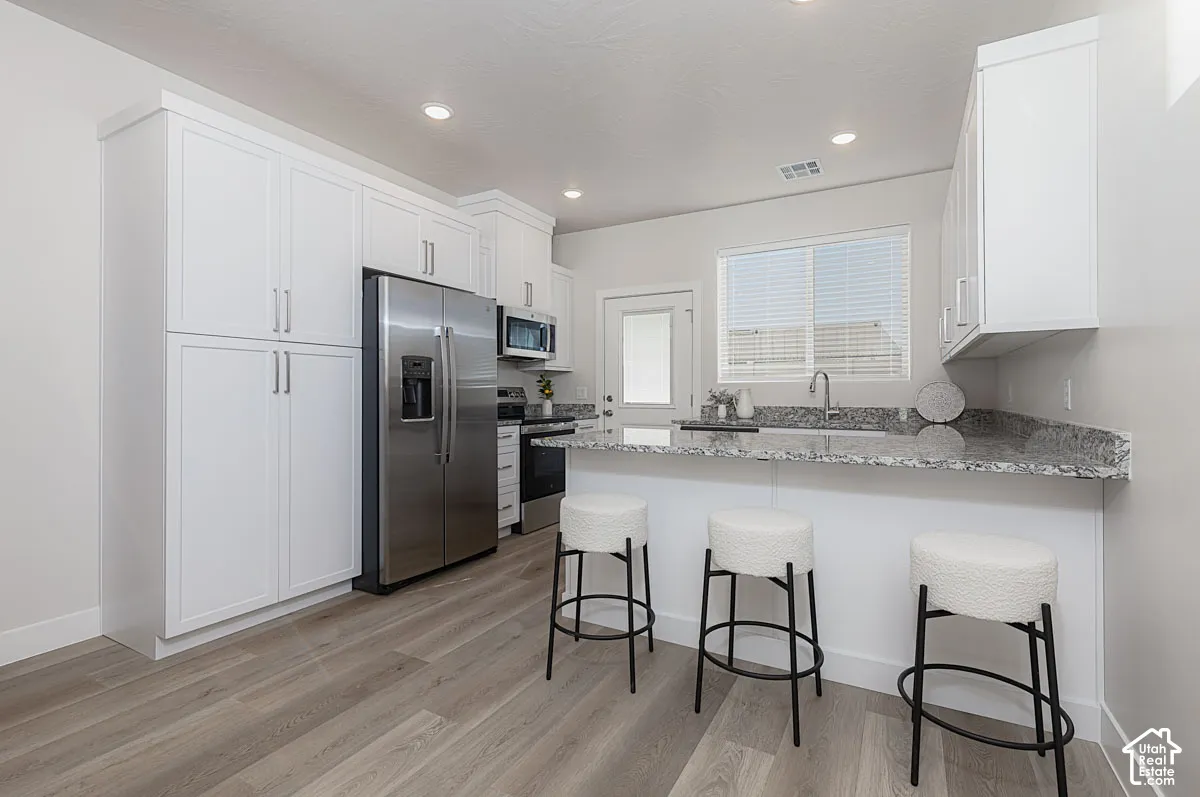 Kitchen featuring a breakfast bar, a peninsula, stainless steel appliances, light stone countertops, and white cabinetry