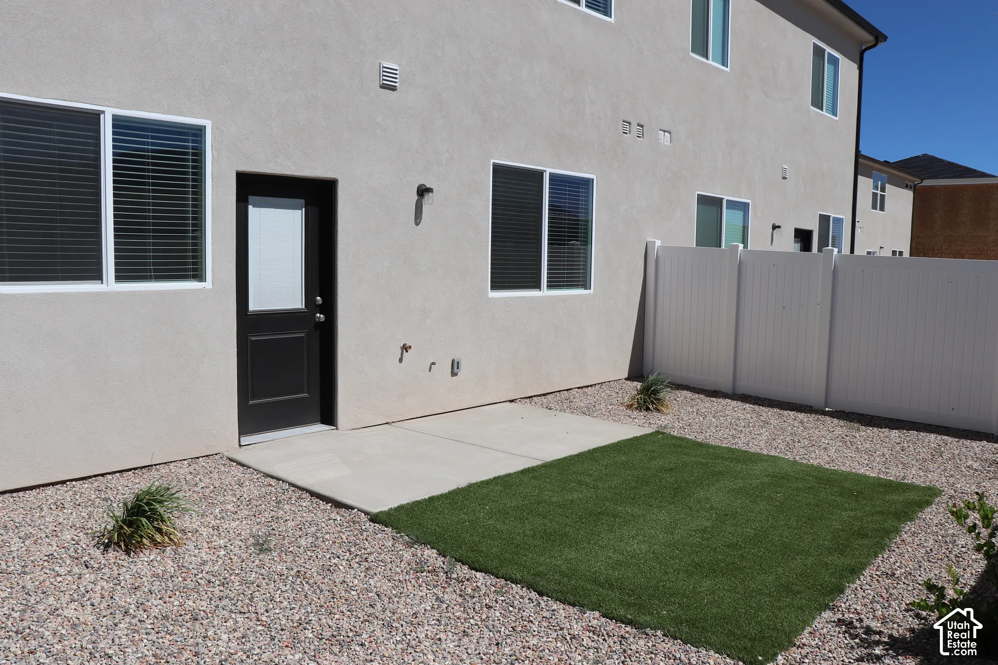 Rear exterior featuring a stucco finish, black panel door with a window, and white-framed windows