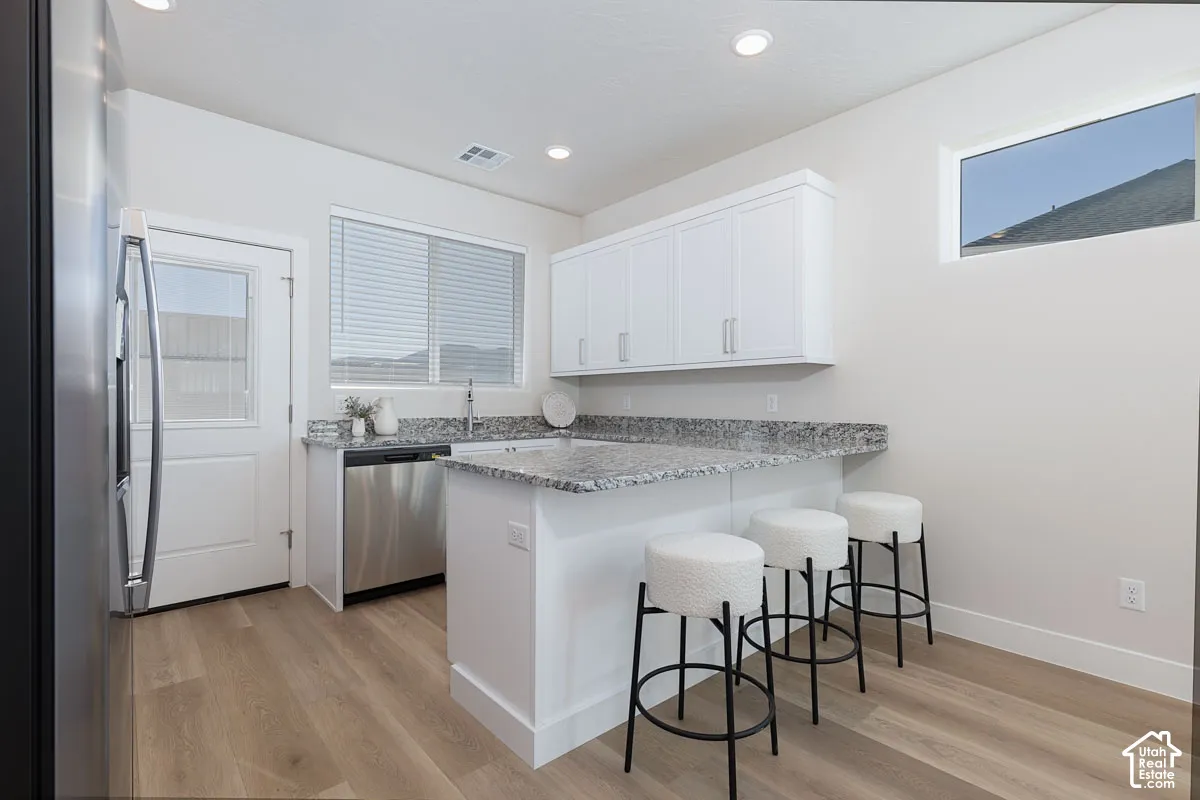 Kitchen featuring stainless steel appliances, a breakfast bar, a peninsula, light wood-style floors, and light stone counters