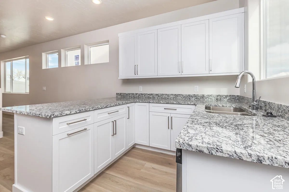 Kitchen featuring a peninsula, light wood-type flooring, white cabinetry, light stone counters, and recessed lighting