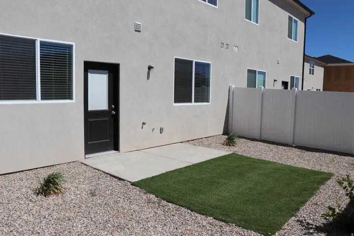 Rear exterior featuring a stucco finish, black panel door with a window, and white-framed windows