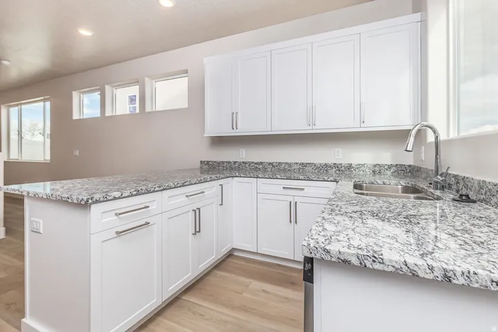 Kitchen featuring a peninsula, light wood-type flooring, white cabinetry, light stone counters, and recessed lighting