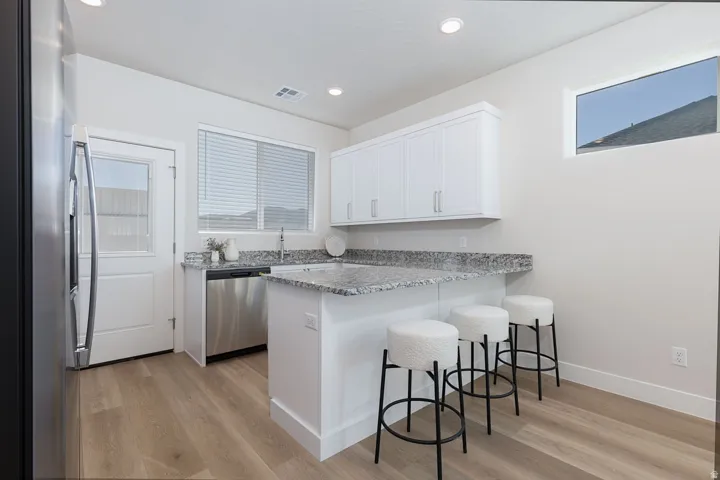Kitchen featuring stainless steel appliances, a breakfast bar, a peninsula, light wood-style floors, and light stone counters