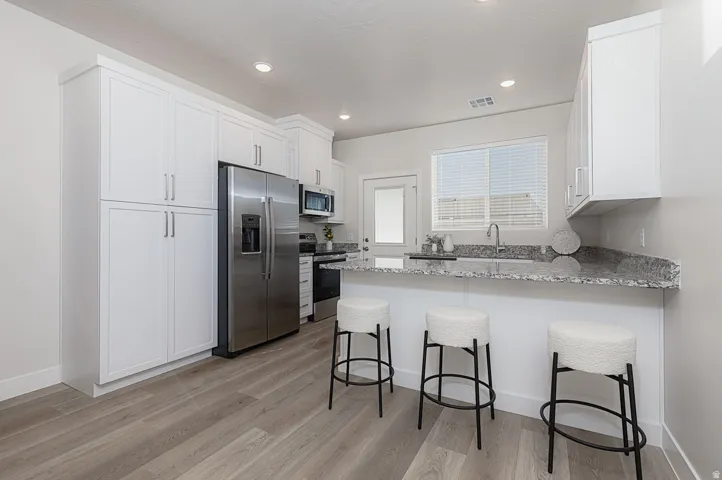 Kitchen featuring a breakfast bar, a peninsula, stainless steel appliances, light stone countertops, and white cabinetry