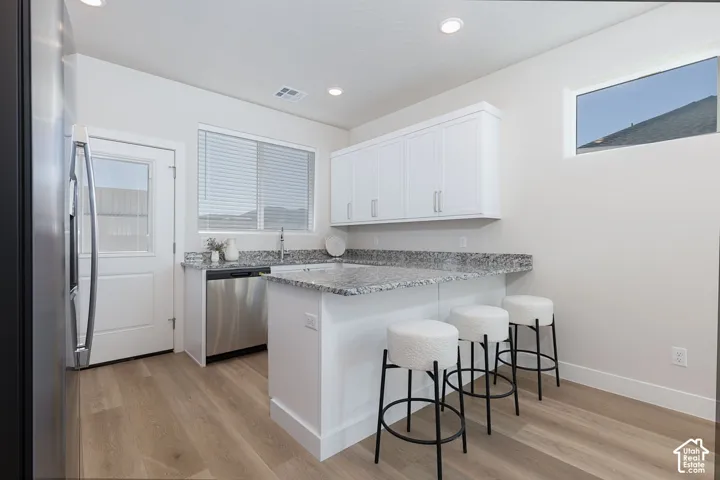 Kitchen featuring stainless steel appliances, a breakfast bar, a peninsula, light wood-style floors, and light stone counters