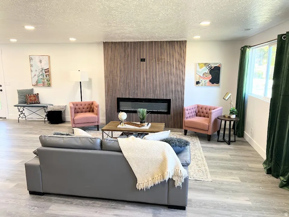 Living room with a glass covered fireplace, a textured ceiling, recessed lighting, and light wood-type flooring