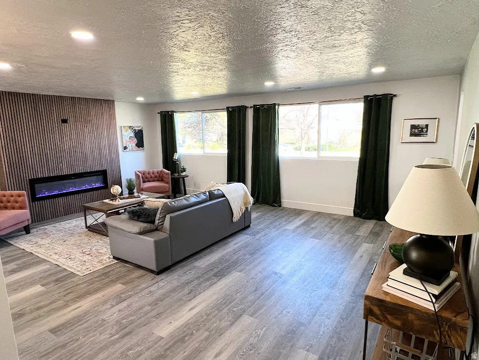 Living area featuring plenty of natural light, a textured ceiling, wood finished floors, recessed lighting, and a glass covered fireplace