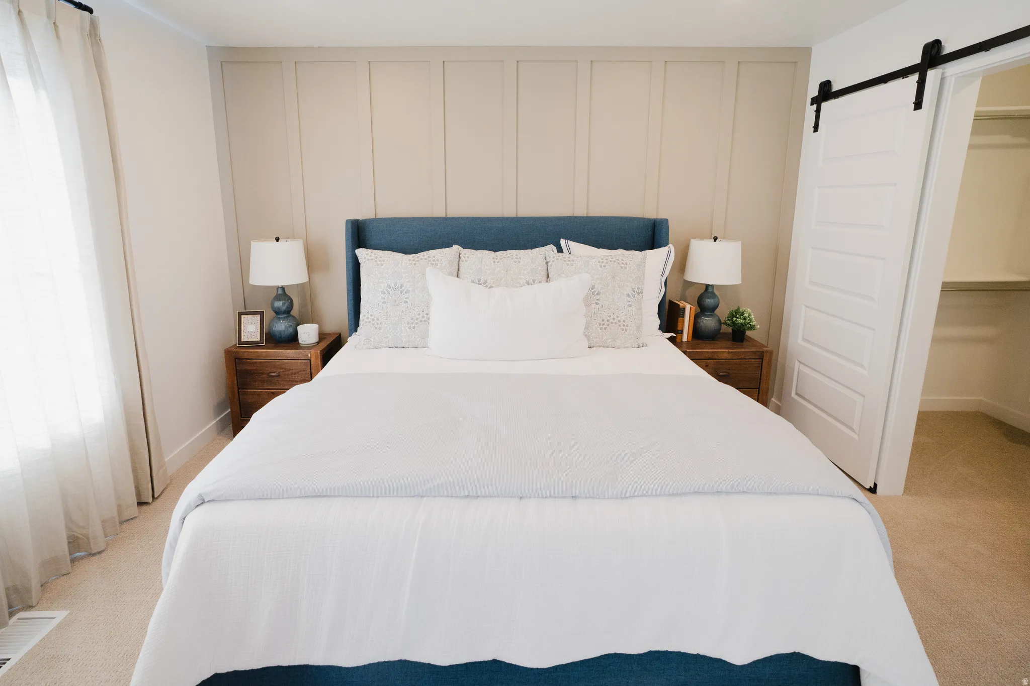 Bedroom with a barn door, light colored carpet, a decorative wall, and a spacious closet