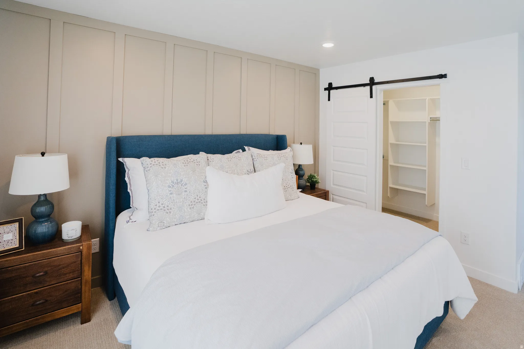 Bedroom with a barn door, light colored carpet, a walk in closet, a decorative wall, and recessed lighting